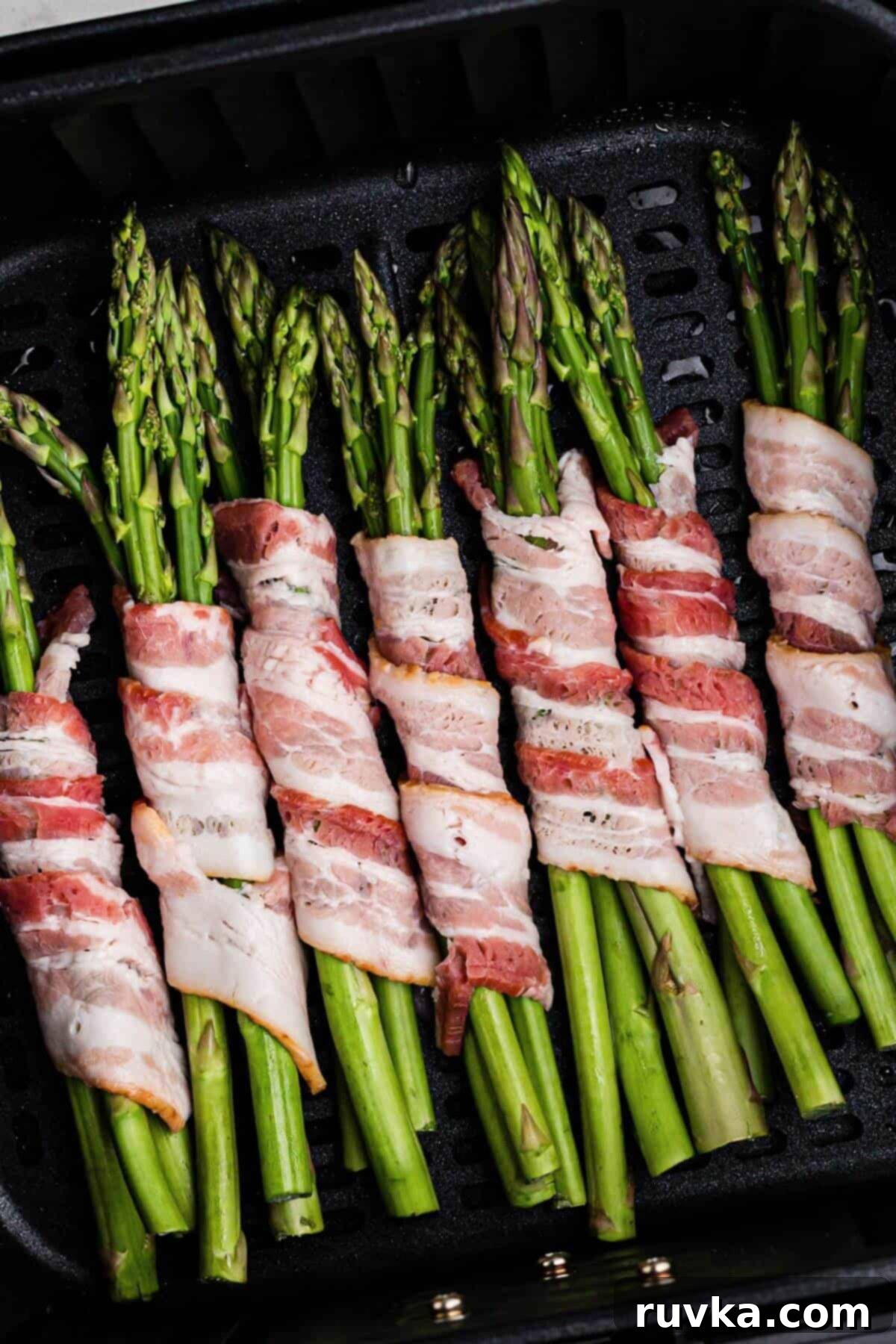 Crispy Air Fryer Bacon Wrapped Asparagus 3 Uncooked bacon wrapped around uncooked asparagus spears in the air fryer basket.