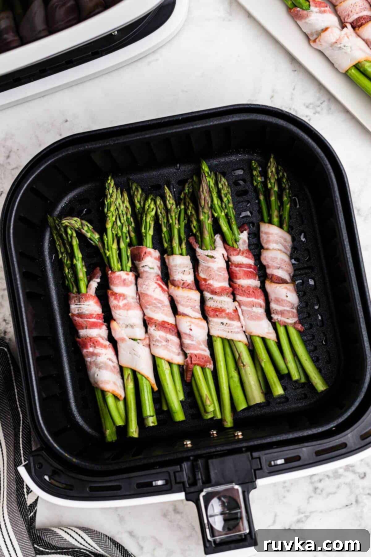 Crispy Air Fryer Bacon Wrapped Asparagus 4 Uncooked bacon slices wrapped around asparagus spears in the air fryer basket.