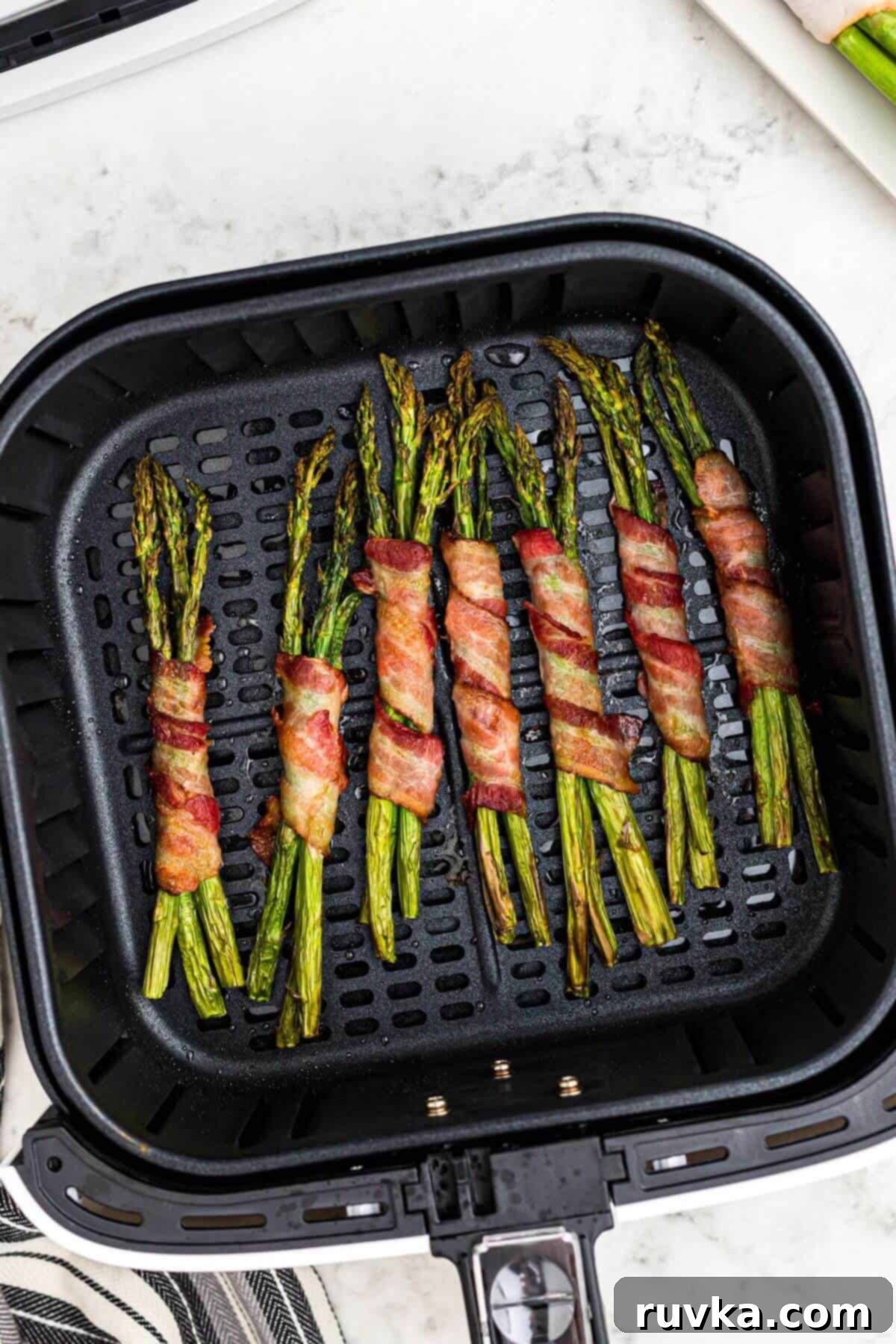 Crispy Air Fryer Bacon Wrapped Asparagus 5 Crispy brown bacon strips wrapped around asparagus stalks in the air fryer basket after being cooked.