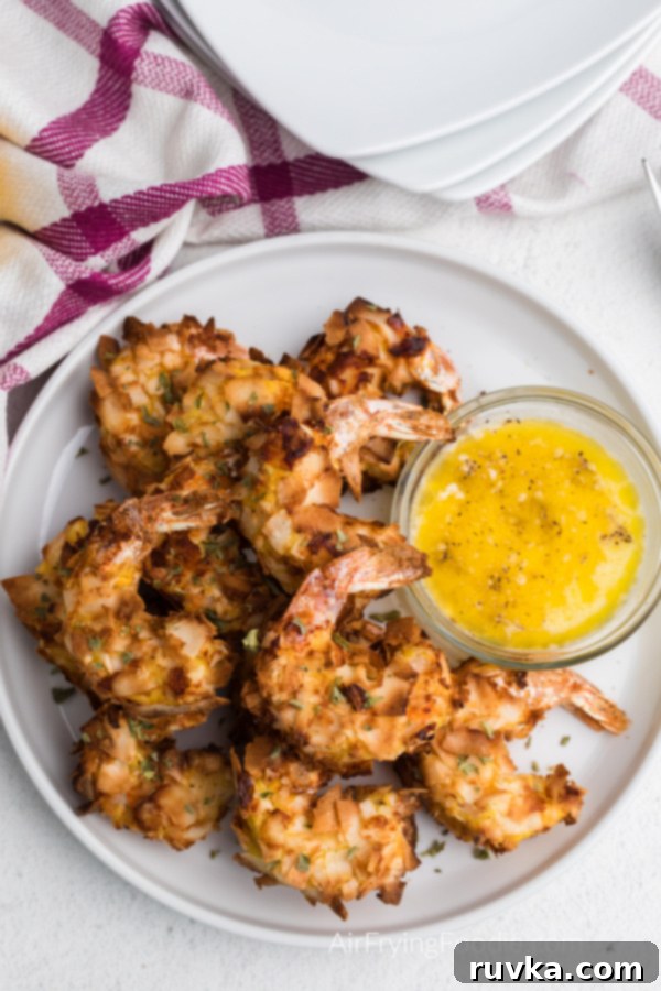 Crispy Air Fryer Keto Coconut Shrimp 3 Air Fried Coconut Shrimp on a white plate with butter sauce for dipping.