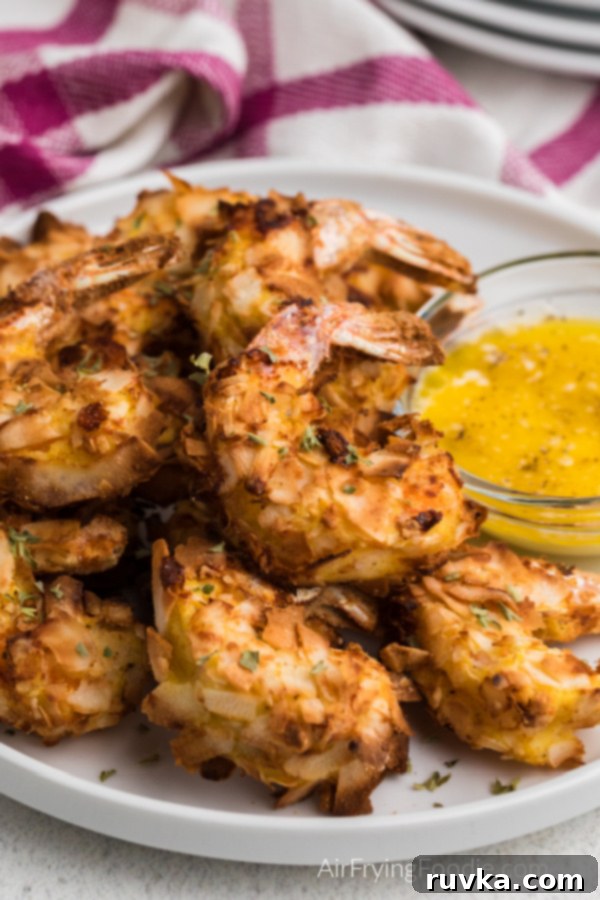 Crispy Air Fryer Keto Coconut Shrimp 10 Close up shop of keto coconut shrimp on a white plate with a buttery dipping sauce on the side.