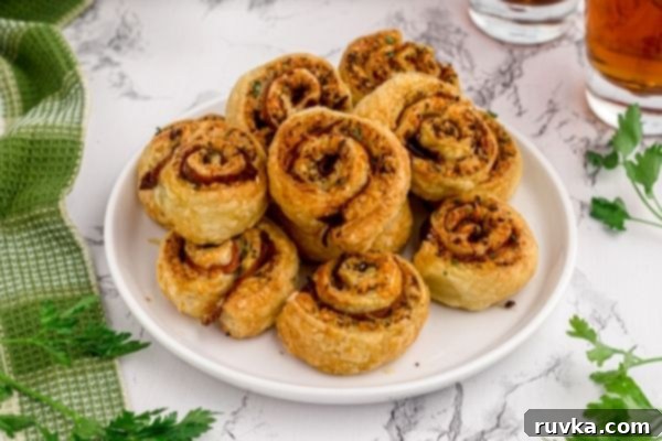 Crispy Air Fryer Pesto Pinwheels 2 Golden, flaky pesto pinwheels piled on a white plate, garnished with fresh parsley.