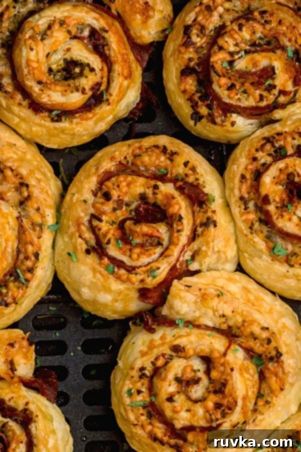 Crispy Air Fryer Pesto Pinwheels 6 Close-up of a perfectly baked golden puff pastry pinwheel, revealing layers of vibrant green pesto, savory ham, and melted parmesan cheese filling.