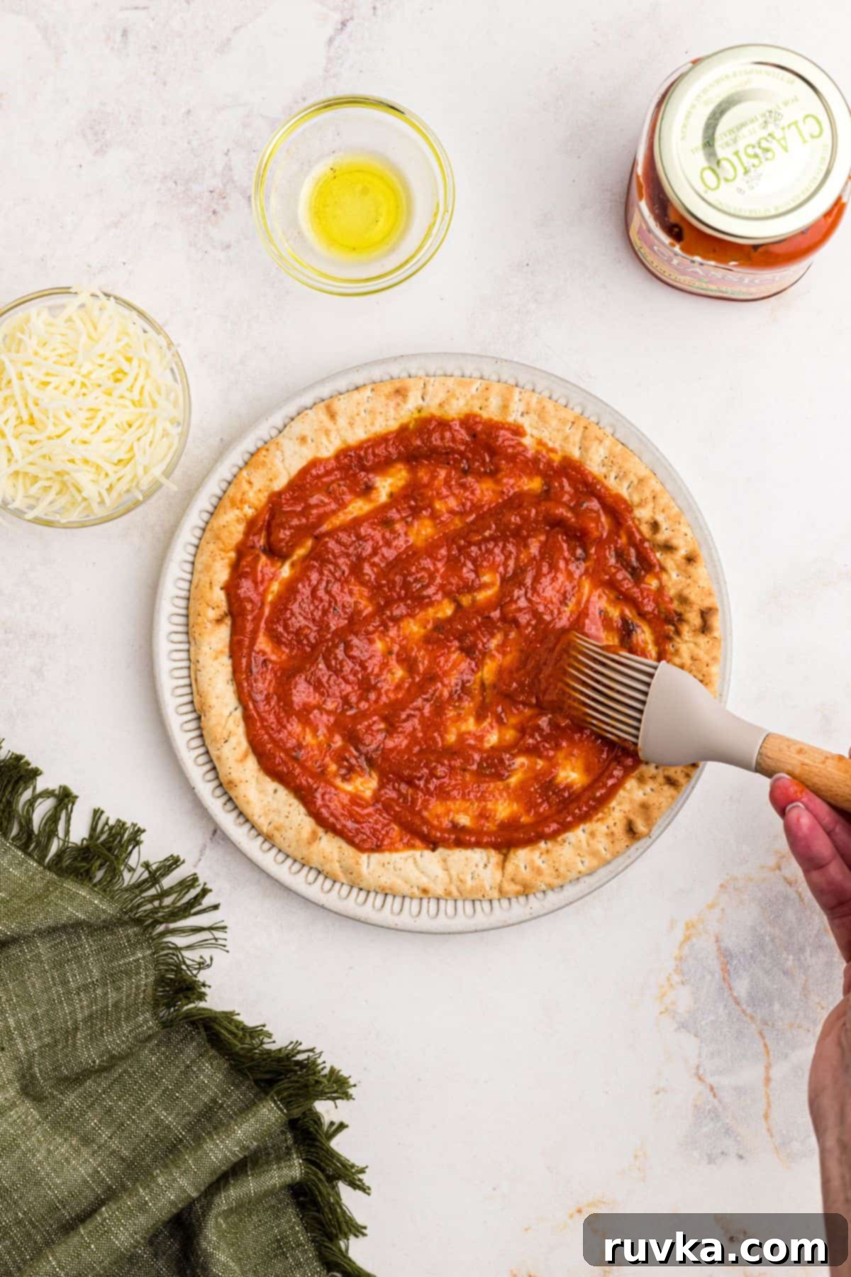 Crispy Air Fryer Pita Pizza 4 Pizza sauce being brushed over a slice of pita bread on a marble table.