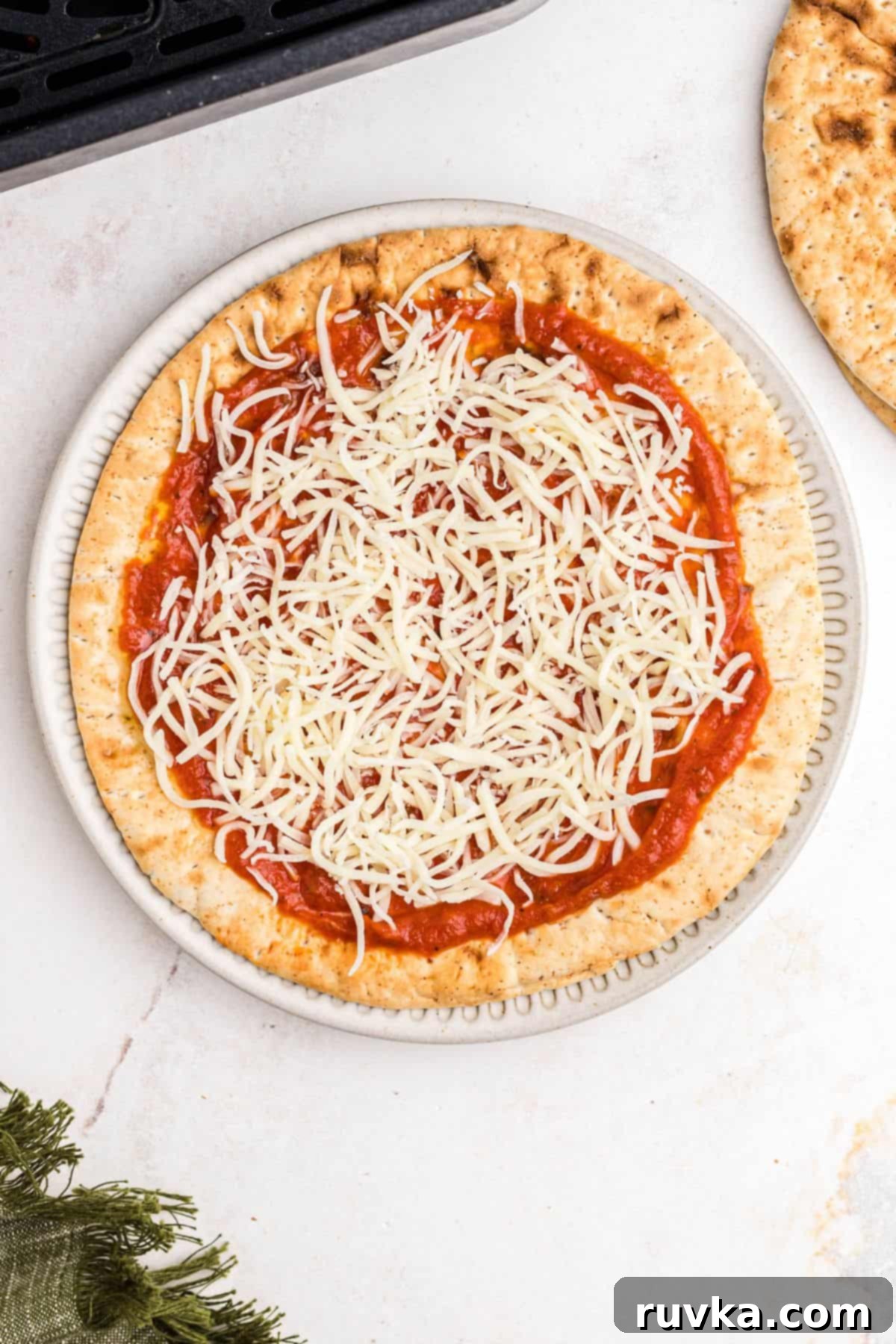 Crispy Air Fryer Pita Pizza 5 Sauce and shredded cheese on pita bread before cooking in the air fryer basket.