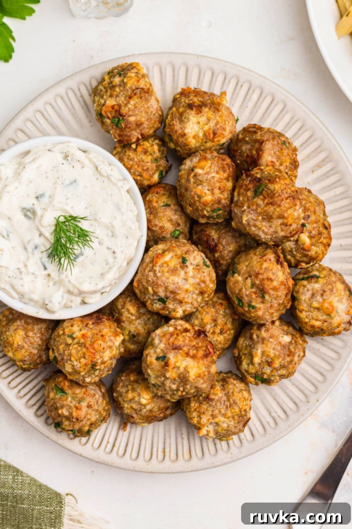 Crispy Air-Fried Greek Meatballs 2 Golden Greek meatballs on a white plate with sauce next to it.