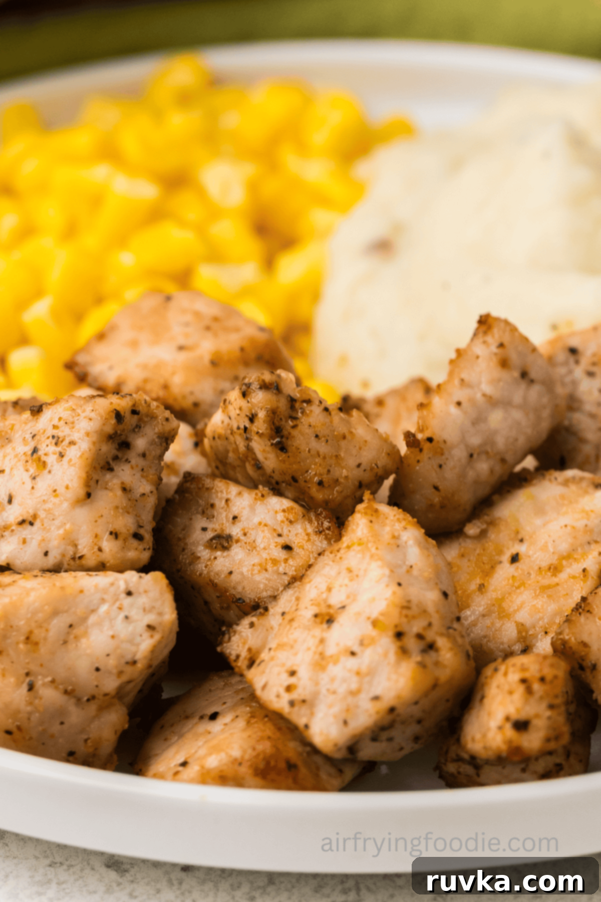 Crispy Air Fryer Pork Cubes 2 Close up of air fried pork chop bites on a plate with corn and mashed potatoes, ready to eat.