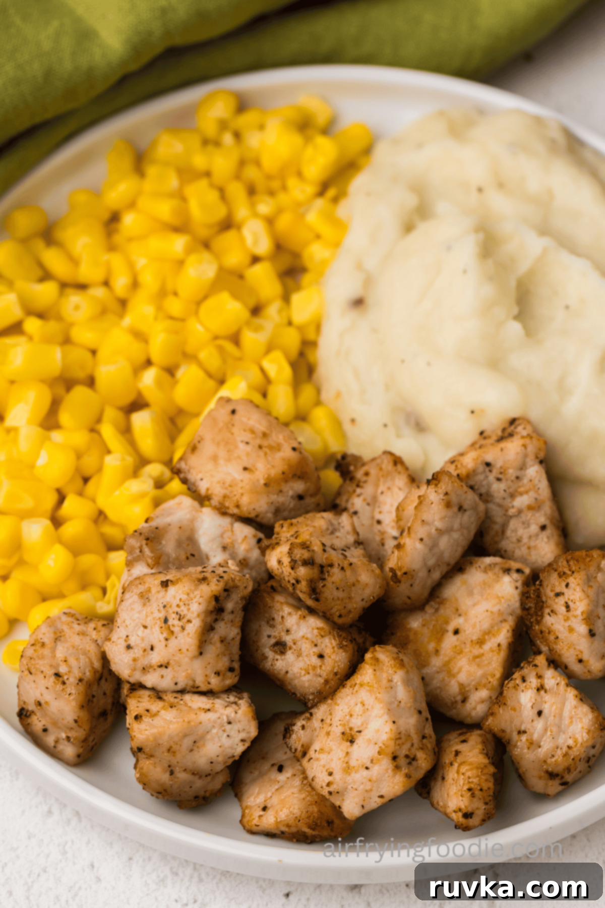 Crispy Air Fryer Pork Cubes 10 Close up of pork chop bites on a plate with corn and mashed potatoes.