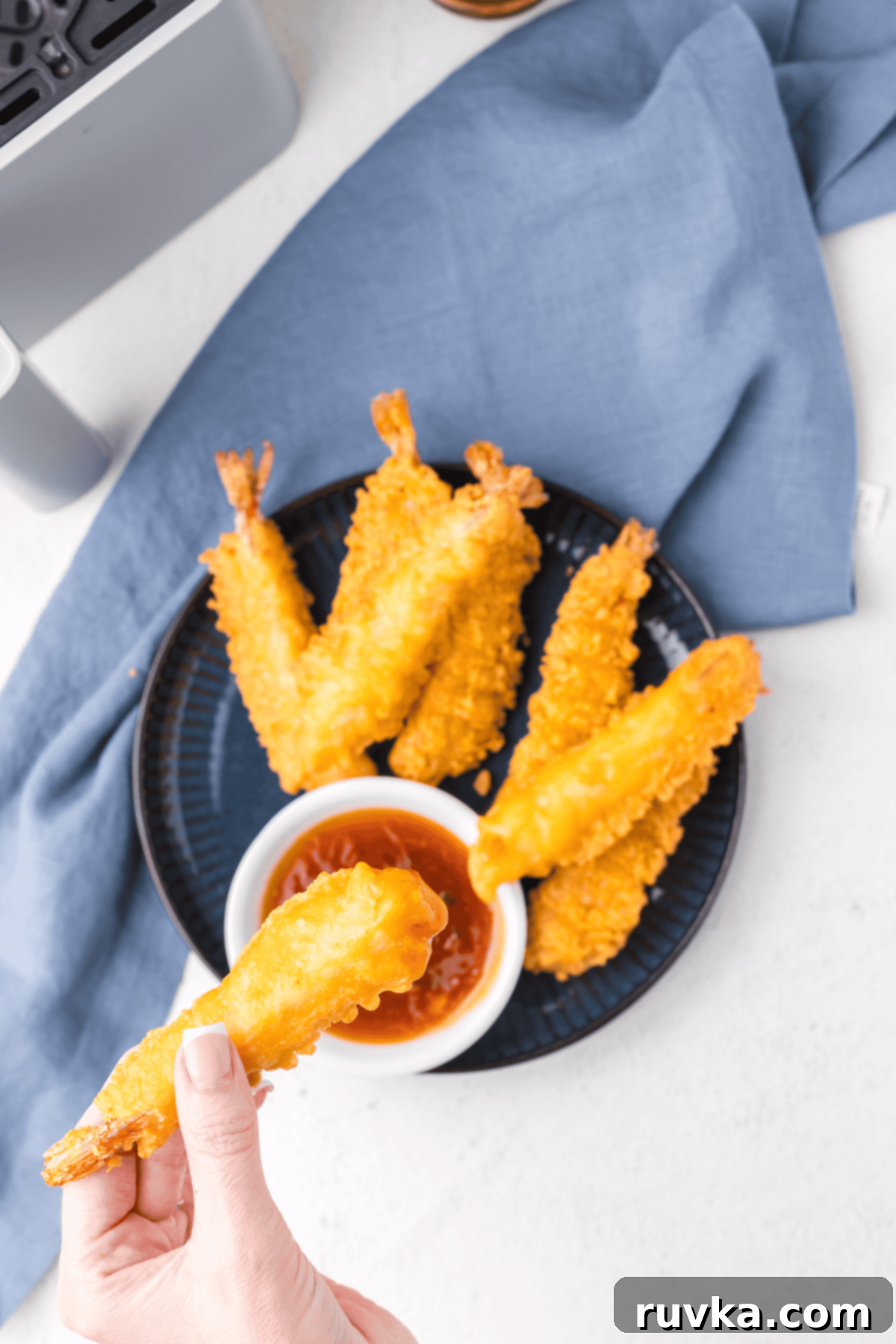 Crispy Air Fryer Frozen Shrimp Tempura 2 Crispy air-fried shrimp tempura served on a plate with one held by hand, ready to be dipped.