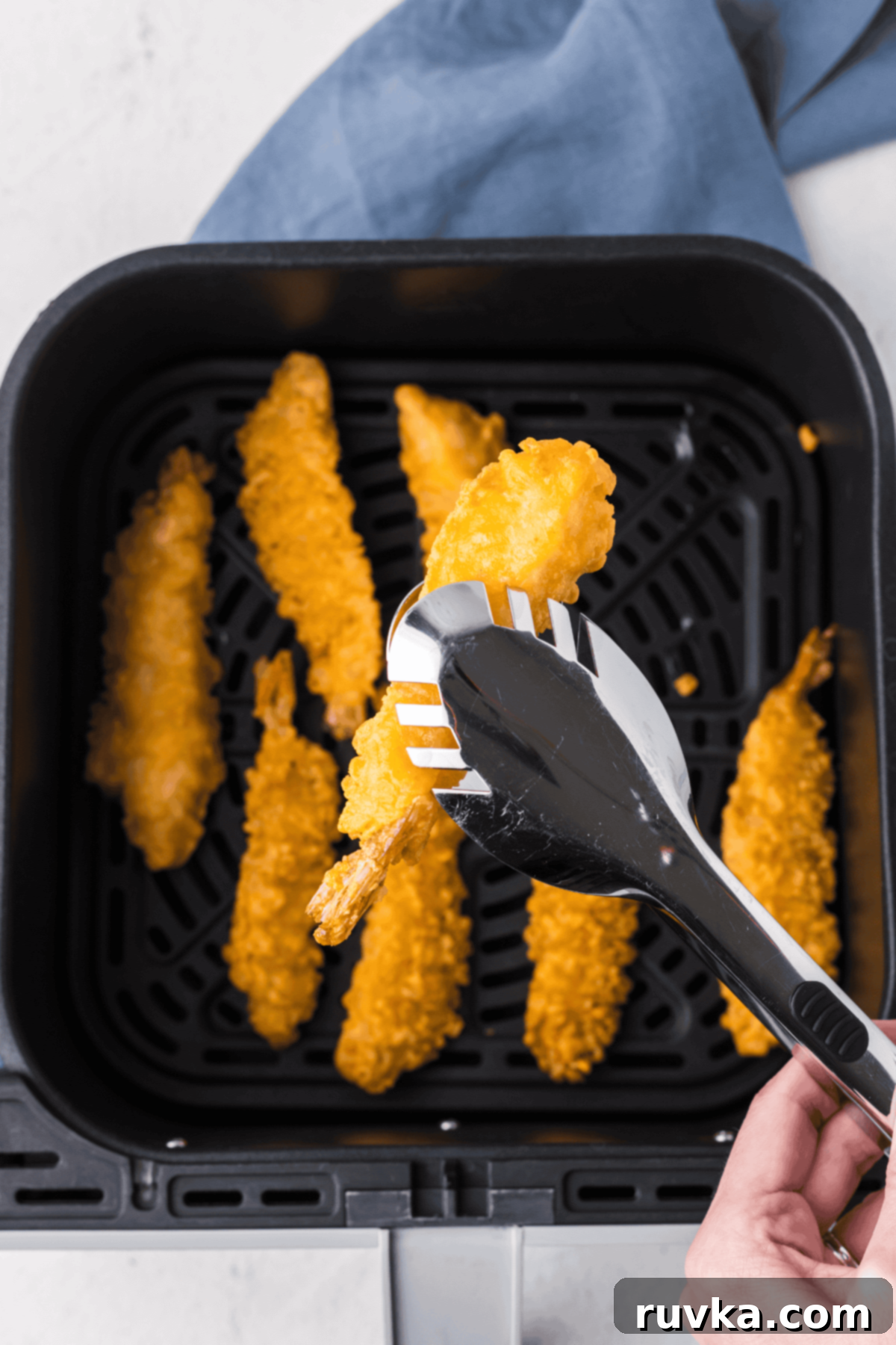 Crispy Air Fryer Frozen Shrimp Tempura 5 Tongs holding a fully cooked, crispy air fryer shrimp tempura over the air fryer basket.