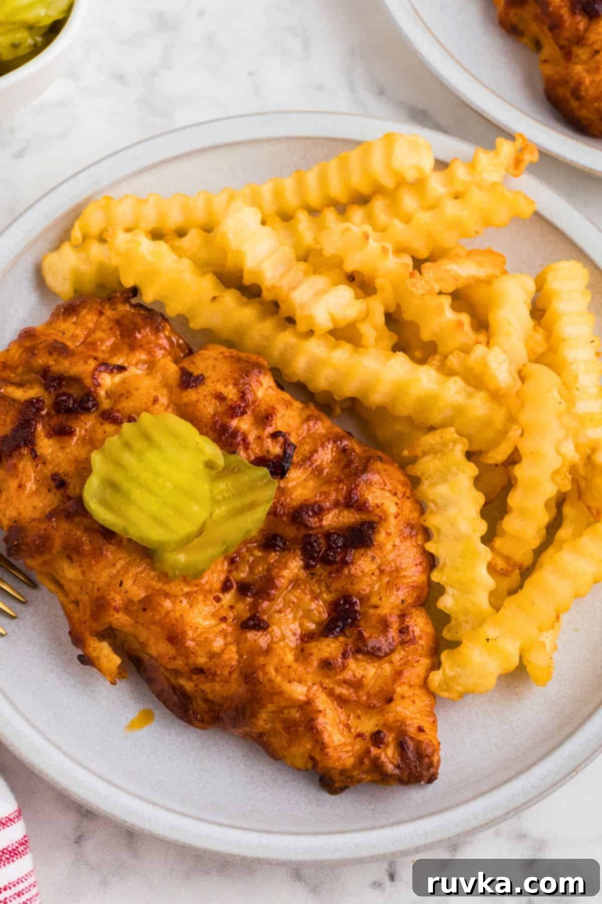 Crispy Air Fryer Nashville Hot Chicken 10 Juicy Nashville hot chicken on a white plate with a side of fries, topped with pickles.