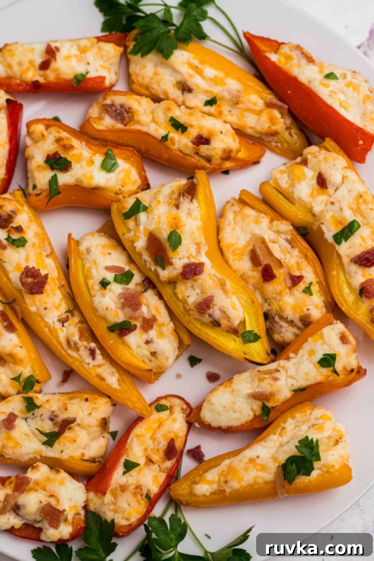 Crispy Air Fryer Stuffed Mini Peppers 2 Red, orange, and yellow mini stuffed peppers on a white plate in front of an air fryer, showcasing their vibrant colors and crispy edges.