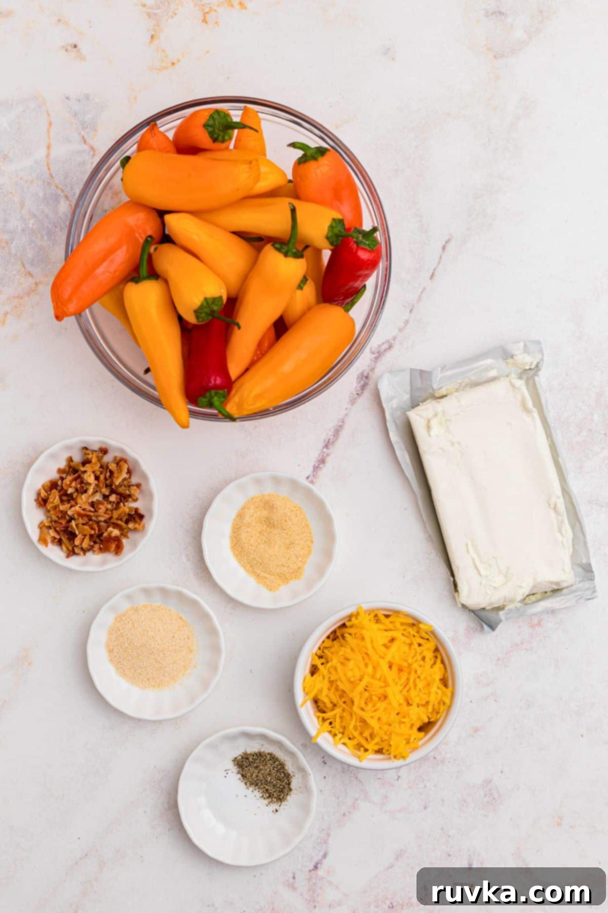 Crispy Air Fryer Stuffed Mini Peppers 3 Ingredients for air fryer stuffed mini peppers, including peppers, cream cheese, cheddar, bacon, and garlic powder, measured into small bowls on a white marble table.