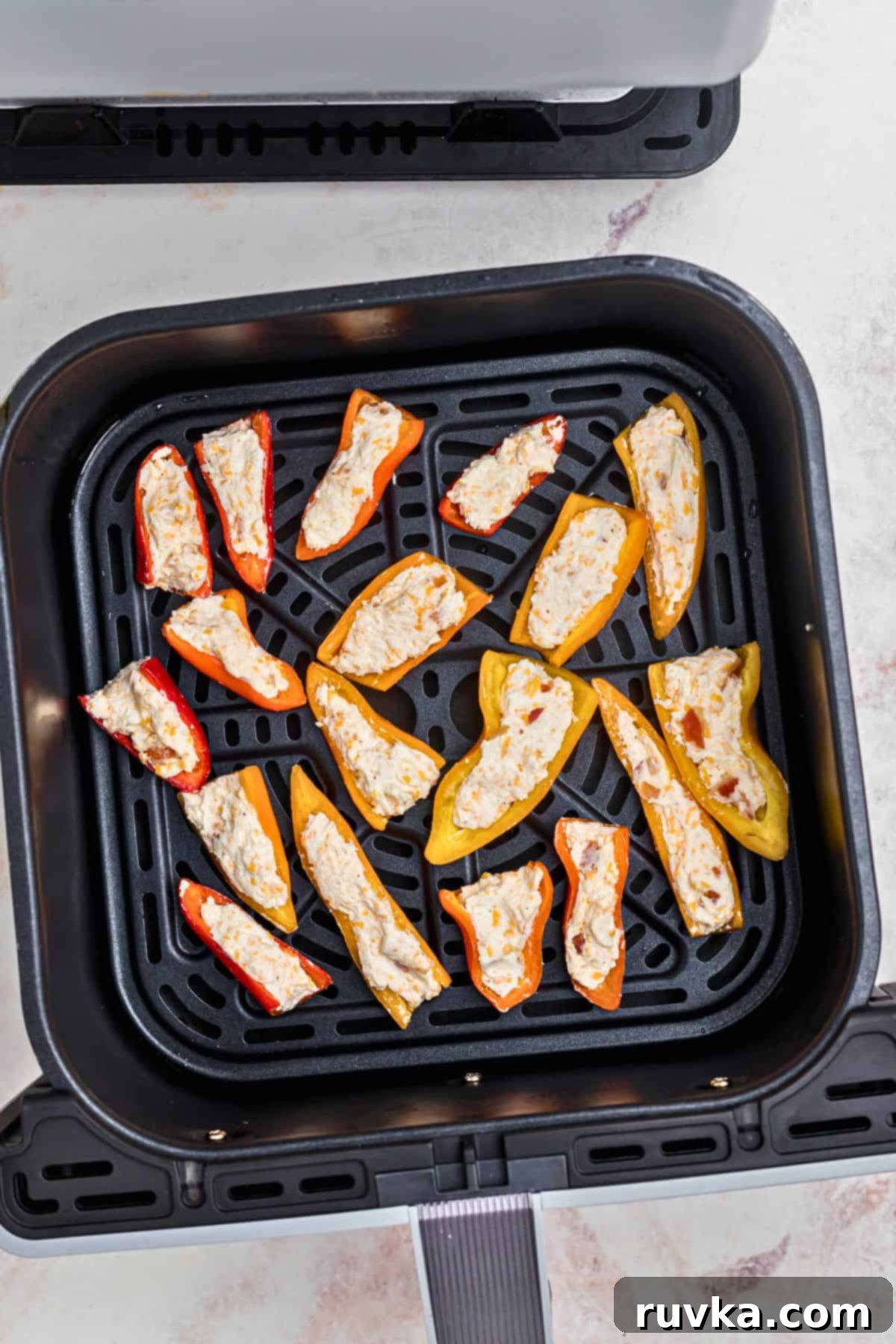 Crispy Air Fryer Stuffed Mini Peppers 6 Mini peppers meticulously stuffed with cream cheese mixture, arranged in a single layer in the air fryer basket, ready for cooking.