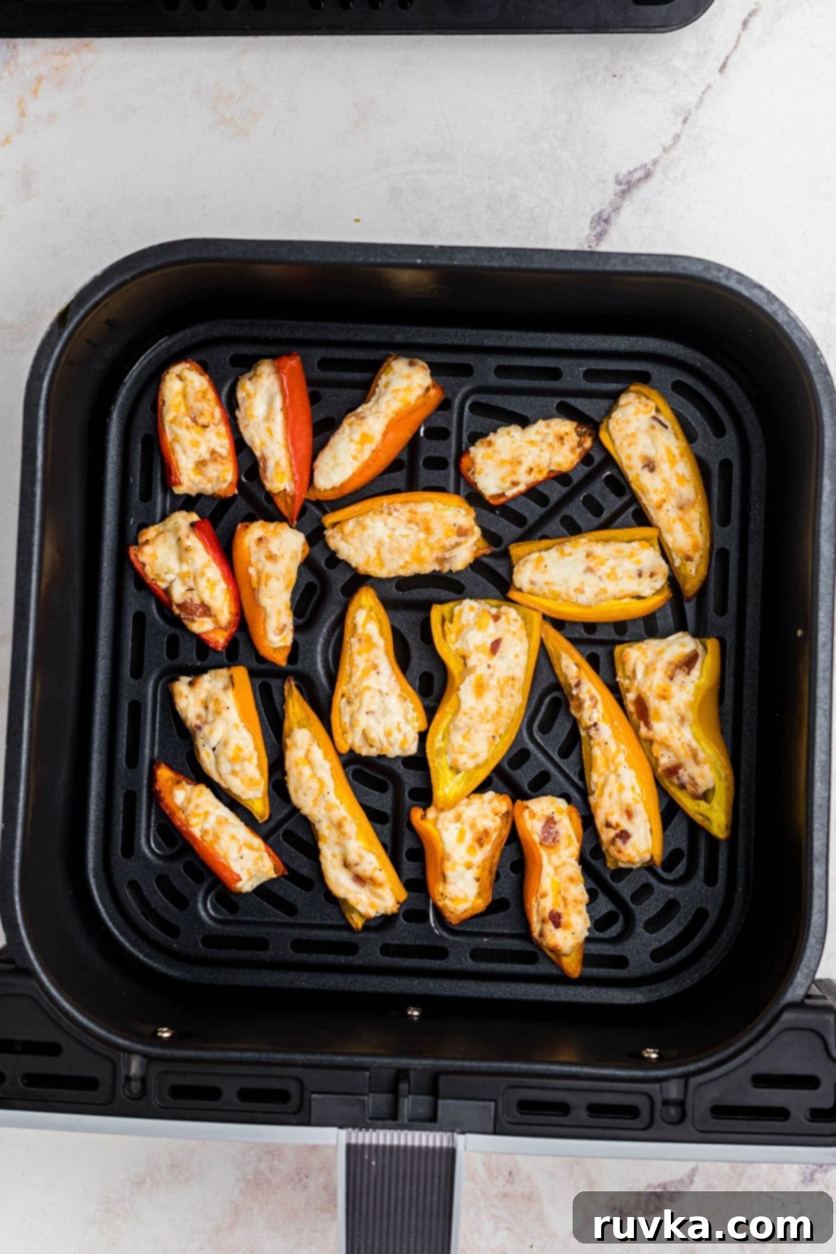 Crispy Air Fryer Stuffed Mini Peppers 7 Mini stuffed peppers, perfectly cooked with golden, bubbly cheese, in the air fryer basket after being cooked.
