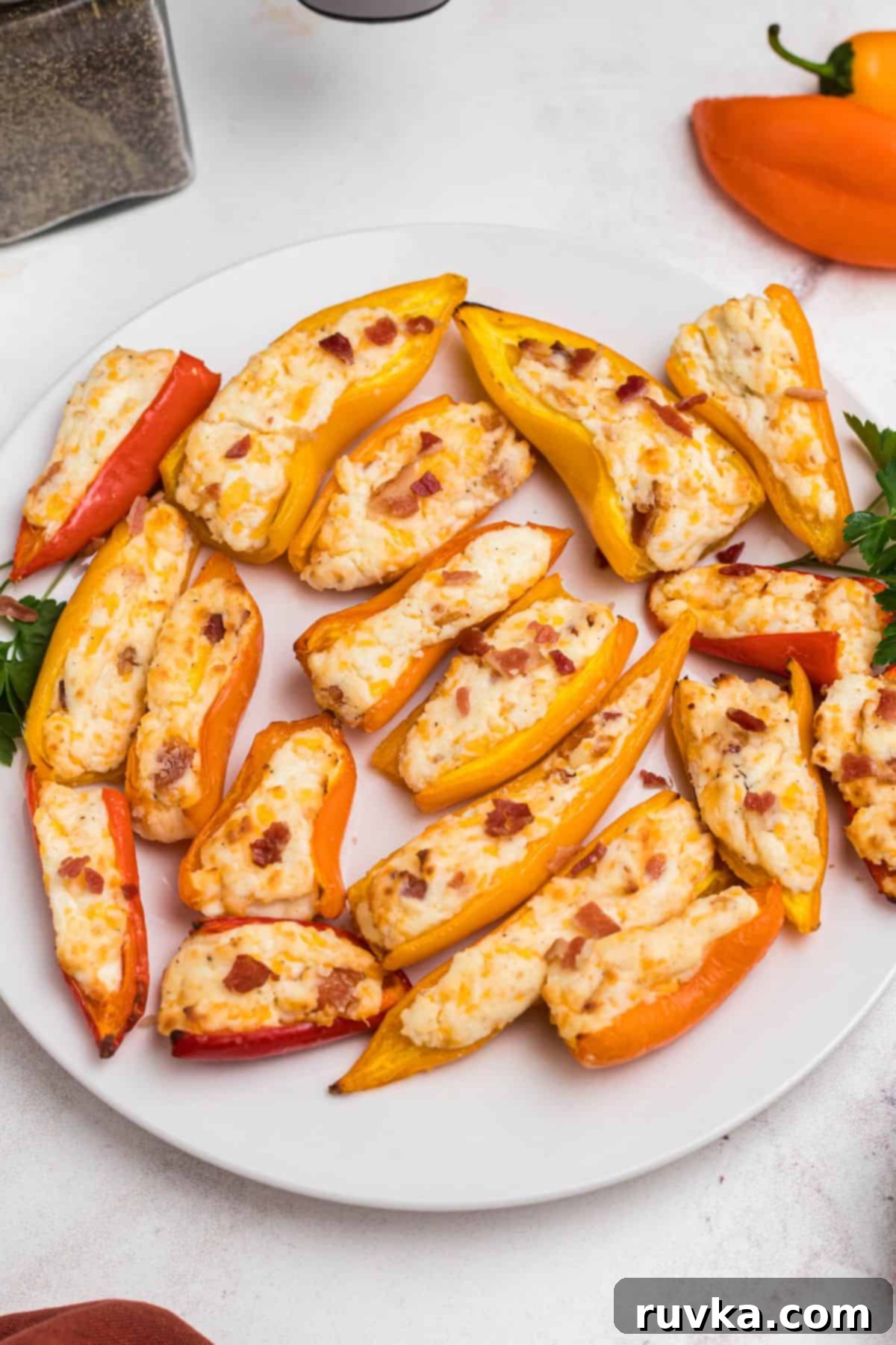 Crispy Air Fryer Stuffed Mini Peppers 8 Red, orange, and yellow mini stuffed peppers artfully arranged on a white plate in front of an air fryer, ready to be enjoyed.