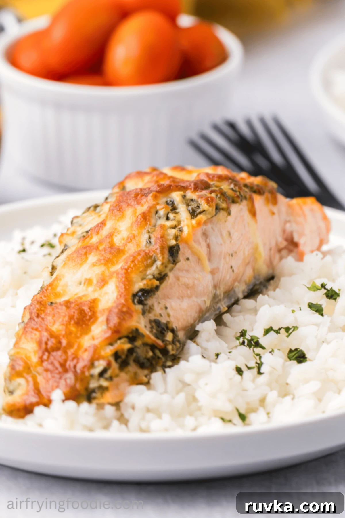 Crispy Air-Fried Pesto Parmesan Salmon 2 Cheesy air fryer pesto salmon on a plate over a bed of rice, garnished with fresh herbs.