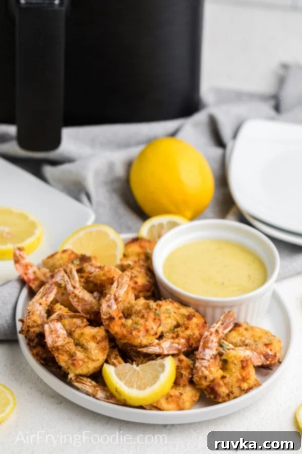 Crispy Keto Air Fryer Shrimp 2 Keto Fried Shrimp made in the air fryer on a white plate with lemon slices and a dipping sauce on the side.