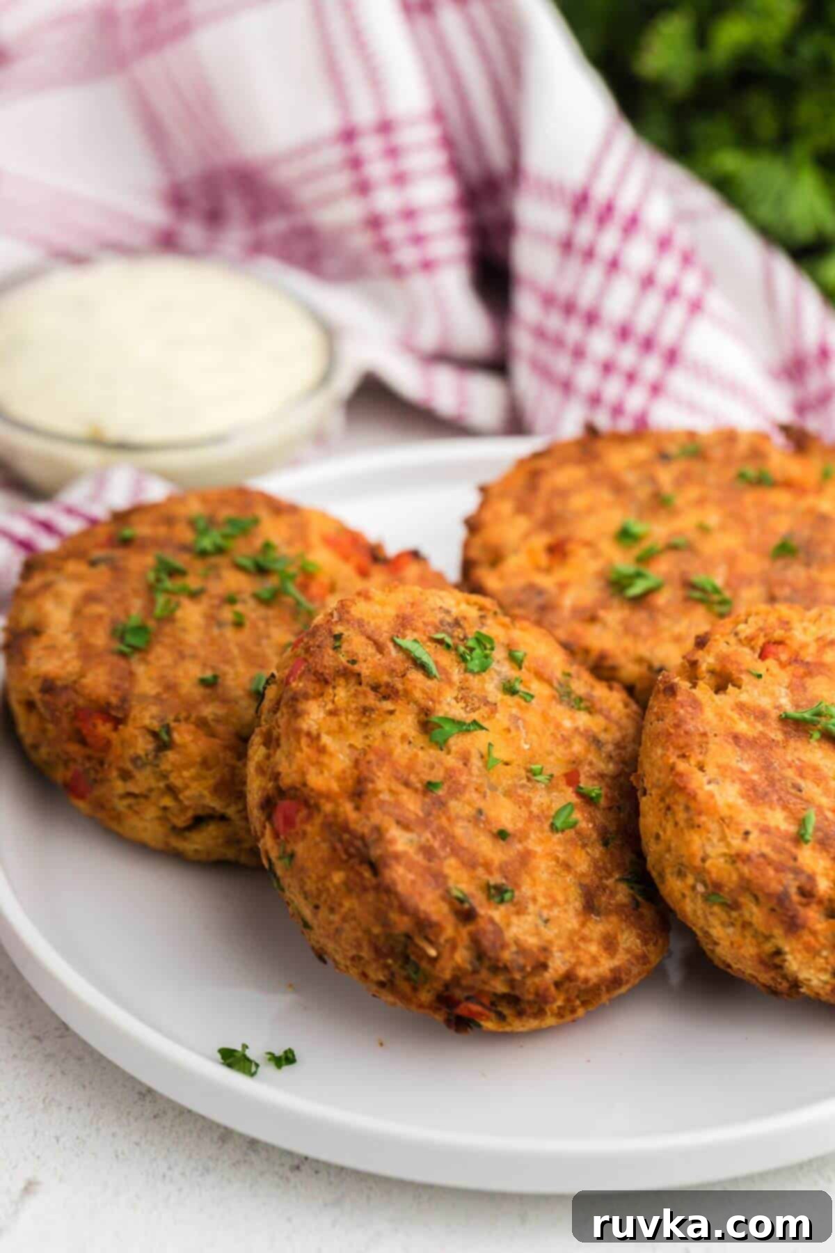 Crispy Air Fryer Salmon Cakes 2 Golden patties on a white plate with a small bowl of tartar sauce.