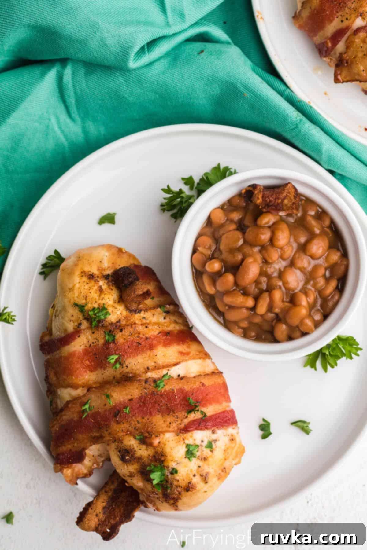 Crispy Air Fryer Bacon Chicken 3 Bacon wrapped chicken on a plate with a small side bowl of beans.