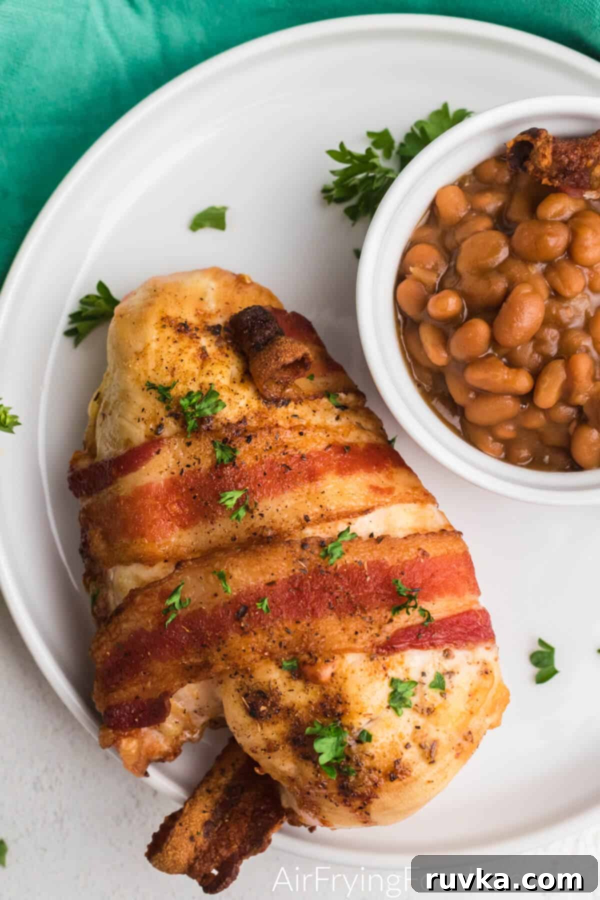 Crispy Air Fryer Bacon Chicken 6 Close up of bacon wrapped chicken on a plate with a side of beans.
