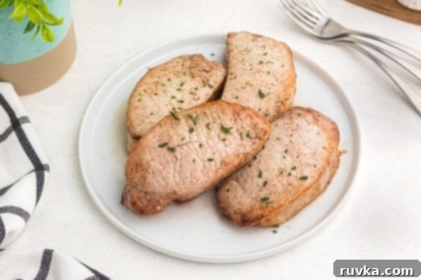 Juicy Air Fryer Maple Glazed Pork Chops 2 Glazed pork chops on a white plate garnished with parsley flakes.