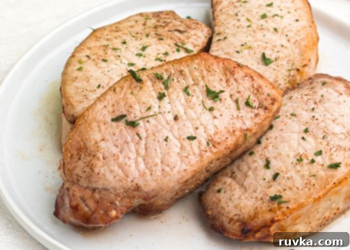 Juicy Air Fryer Maple Glazed Pork Chops 6 Close up photo of cooked chops stacked and served on a white plate with parsley flakes as a garnish