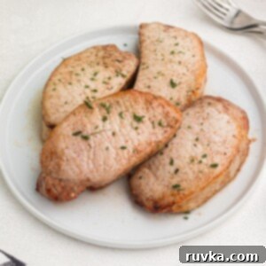 Juicy Air Fryer Maple Glazed Pork Chops 7 Cooked glazed pork chops cooked and served on a white plate, sprinkled with parsley flakes.