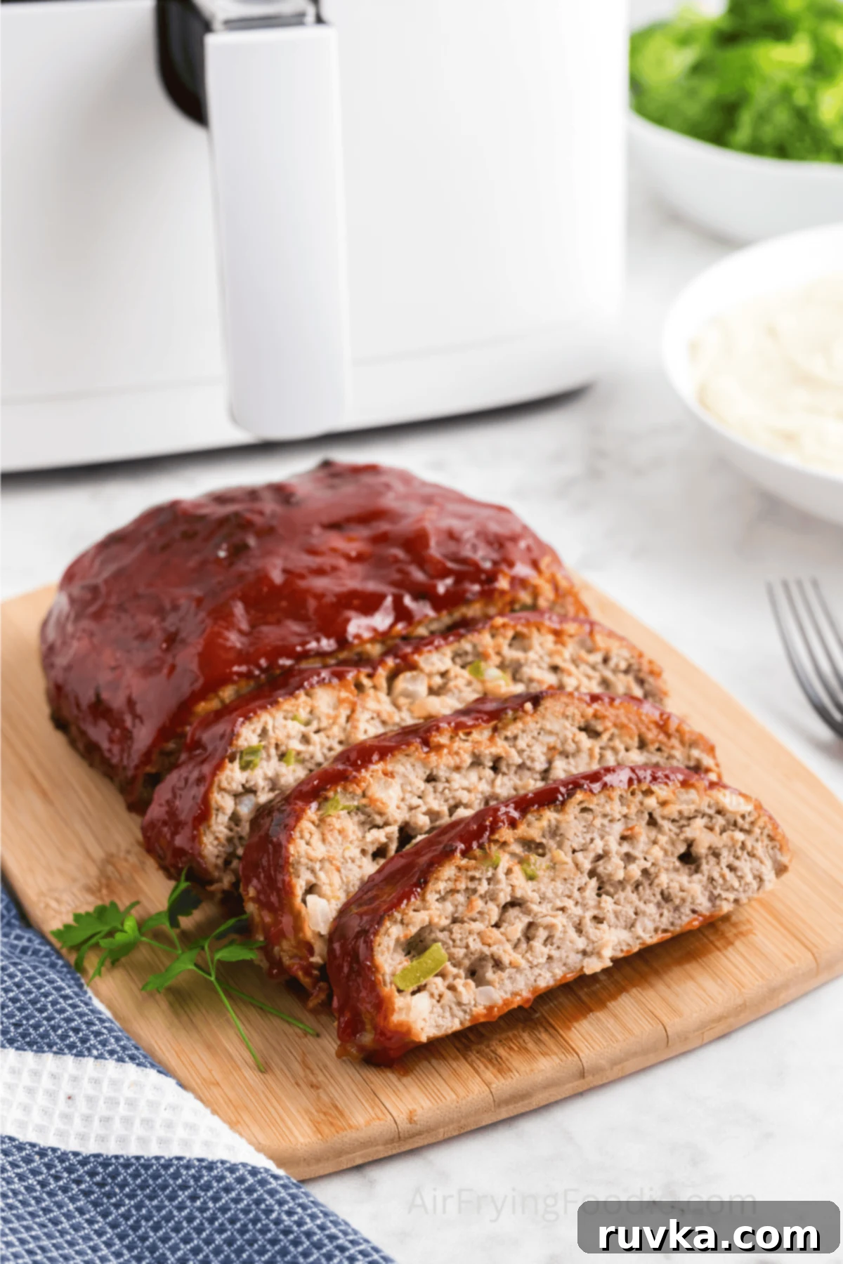 Turkey meatloaf air fried and sliced on a cutting board on a table in front of an air fryer.