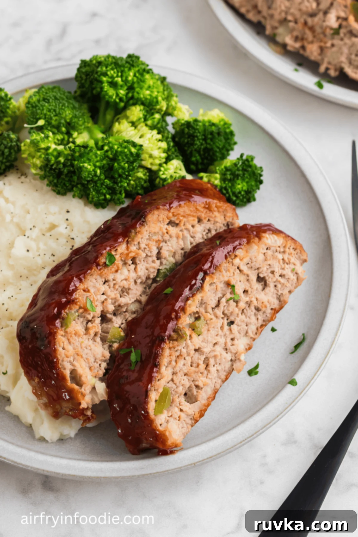 Sliced air frried turkey meatloaf on a plate with mashed potatoes and a side of broccoli. 