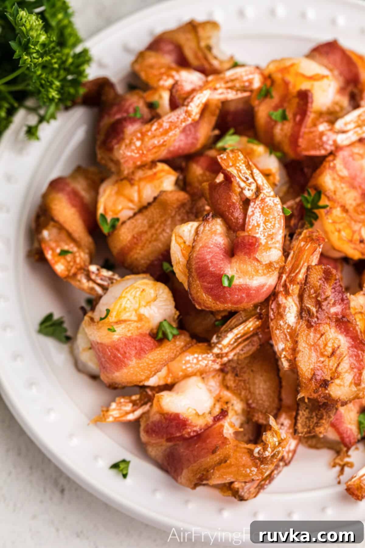 Crispy Air Fryer Bacon Wrapped Shrimp 2 Delicious Air Fryer Bacon Wrapped Shrimp served on a white plate, garnished with fresh parsley.