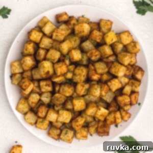 Crispy Air Fryer Breakfast Spuds 8 golden cubes of potatoes cut and cooked served on a white plate and garnished with parsley.