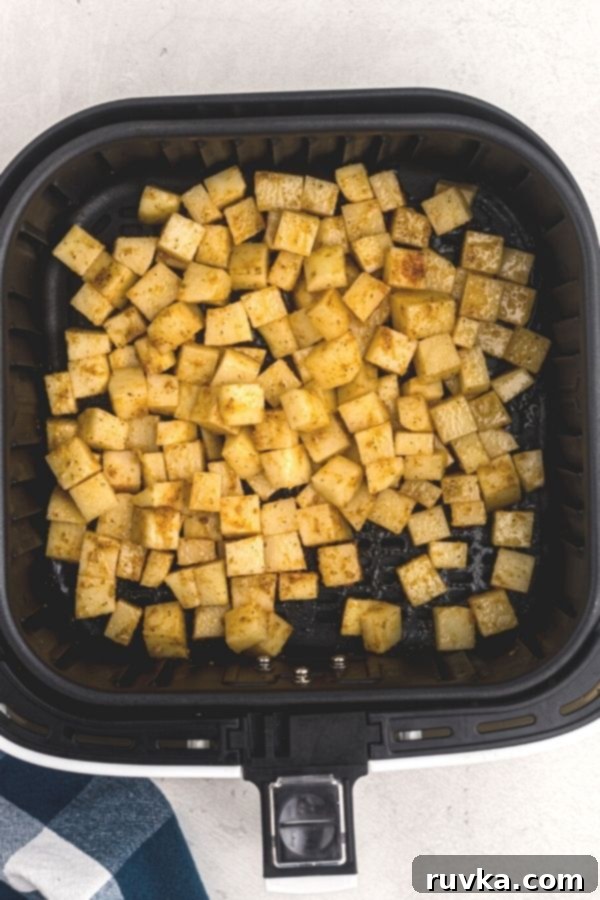 Crispy Air Fryer Breakfast Spuds 4 Soaked and seasoned cubes of potatoes, in an air fryer basket. Uncooked.