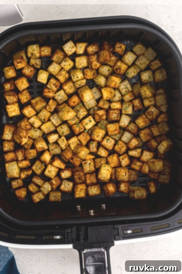 Crispy Air Fryer Breakfast Spuds 5 Golden, seasoned cubes of potatoes, in an air fryer basket after being cooked.