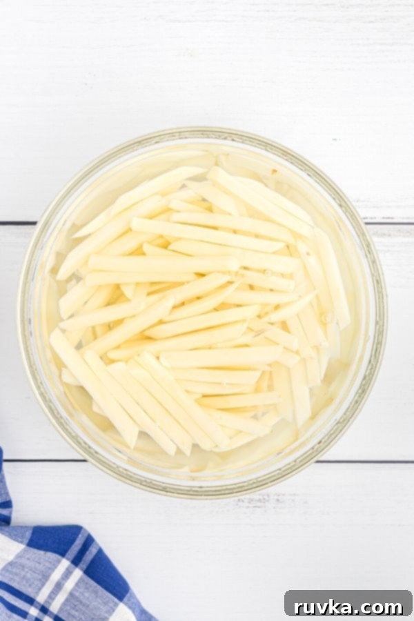 Crispy Air Fryer Seasoned Fries 4 Slices of potatoes soaking in a cold water in a glass bowl.