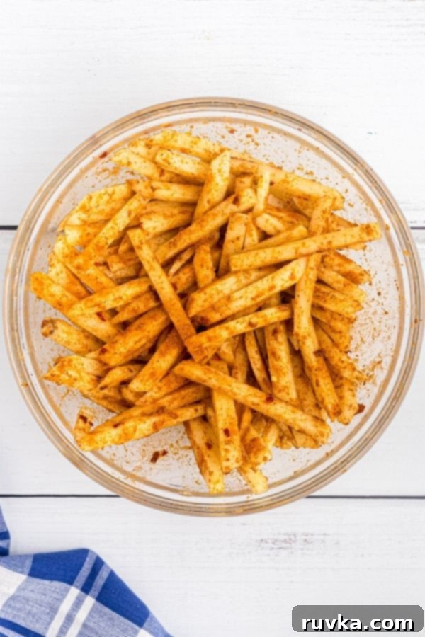 Crispy Air Fryer Seasoned Fries 5 Slices of potatoes in a glass bowl, tossed with olive oil and seasonings.
