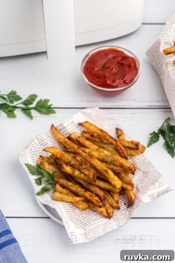 Crispy Air Fryer Seasoned Fries 7 Serving of golden fries served on a white plate with paper and fresh parsley on the table.