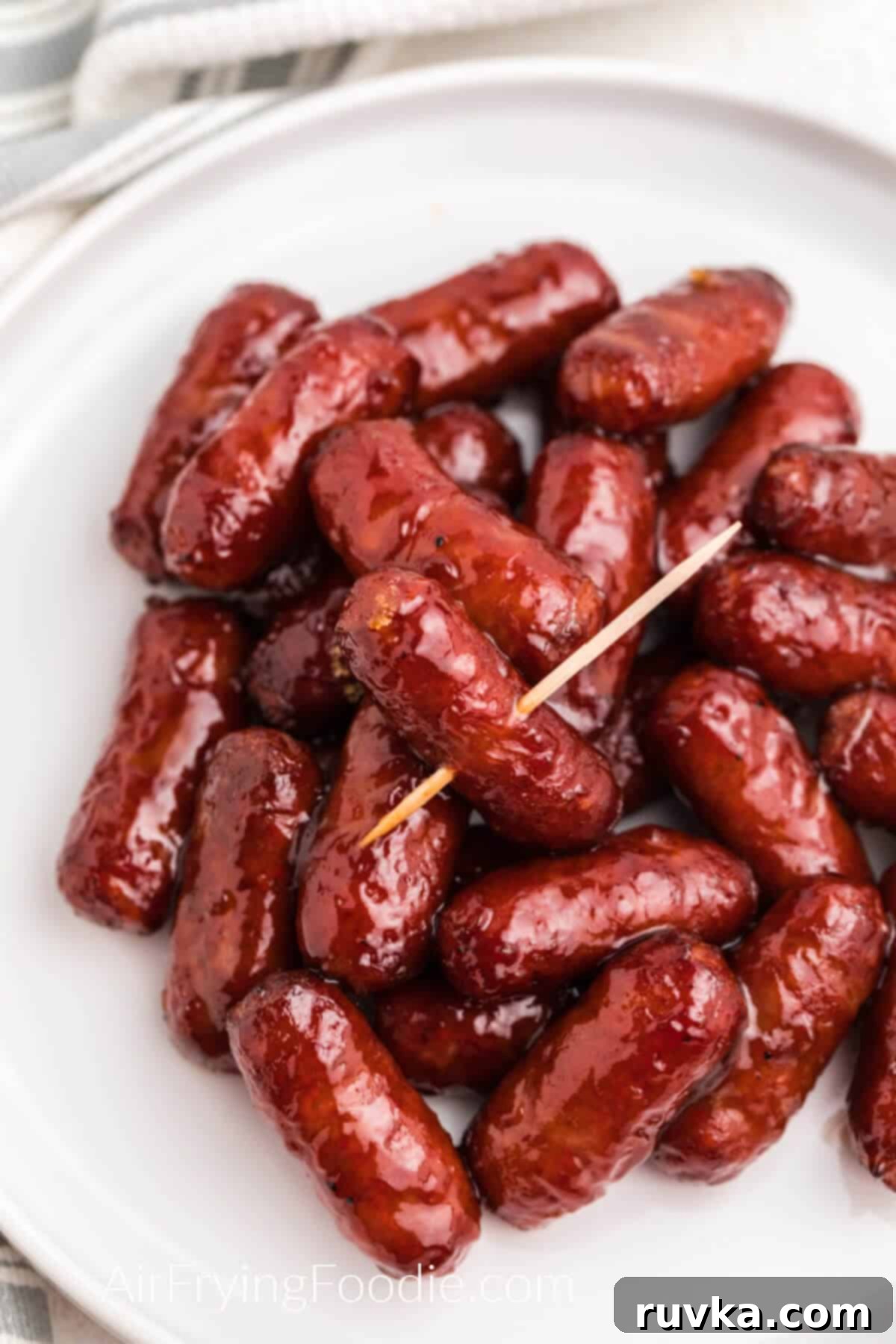 Easy Air Fryer BBQ Little Smokies 2 bbq lil smokies on a white plate, made in the air fryer, one with a toothpick stuck through it. Ready to eat.