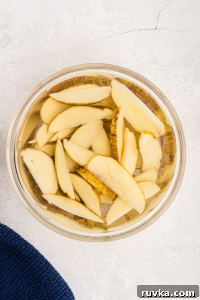 Crispy Air Fryer Potato Wedges 4 Clear glass bowl filled with ice water, with potato wedges soaking.