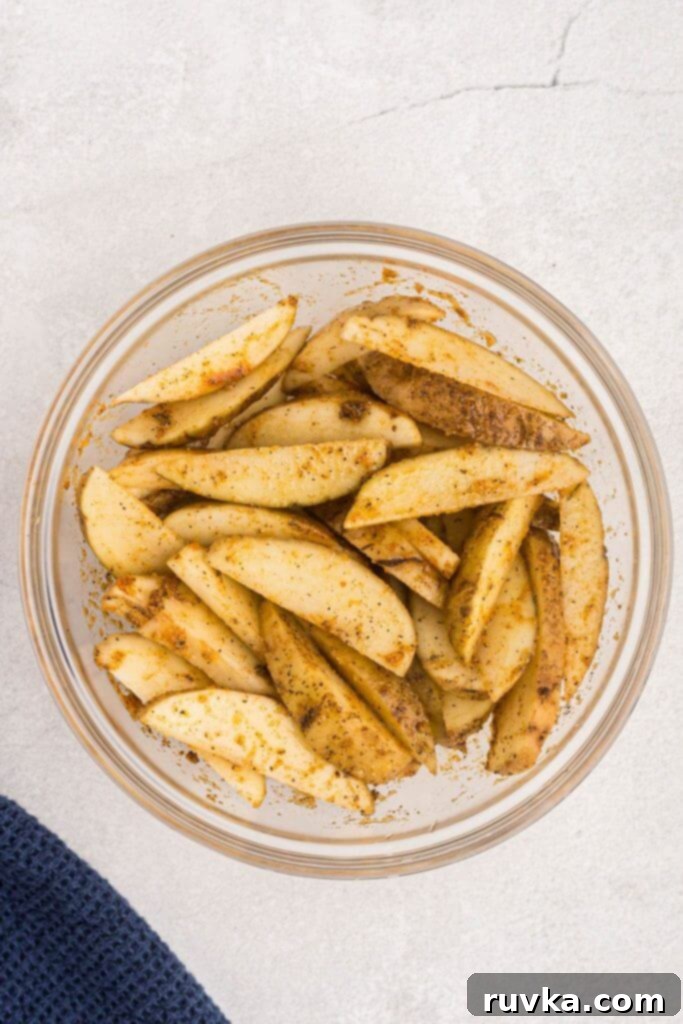 Crispy Air Fryer Potato Wedges 5 Uncooked potato wedges seasoned in a clear glass bowl.