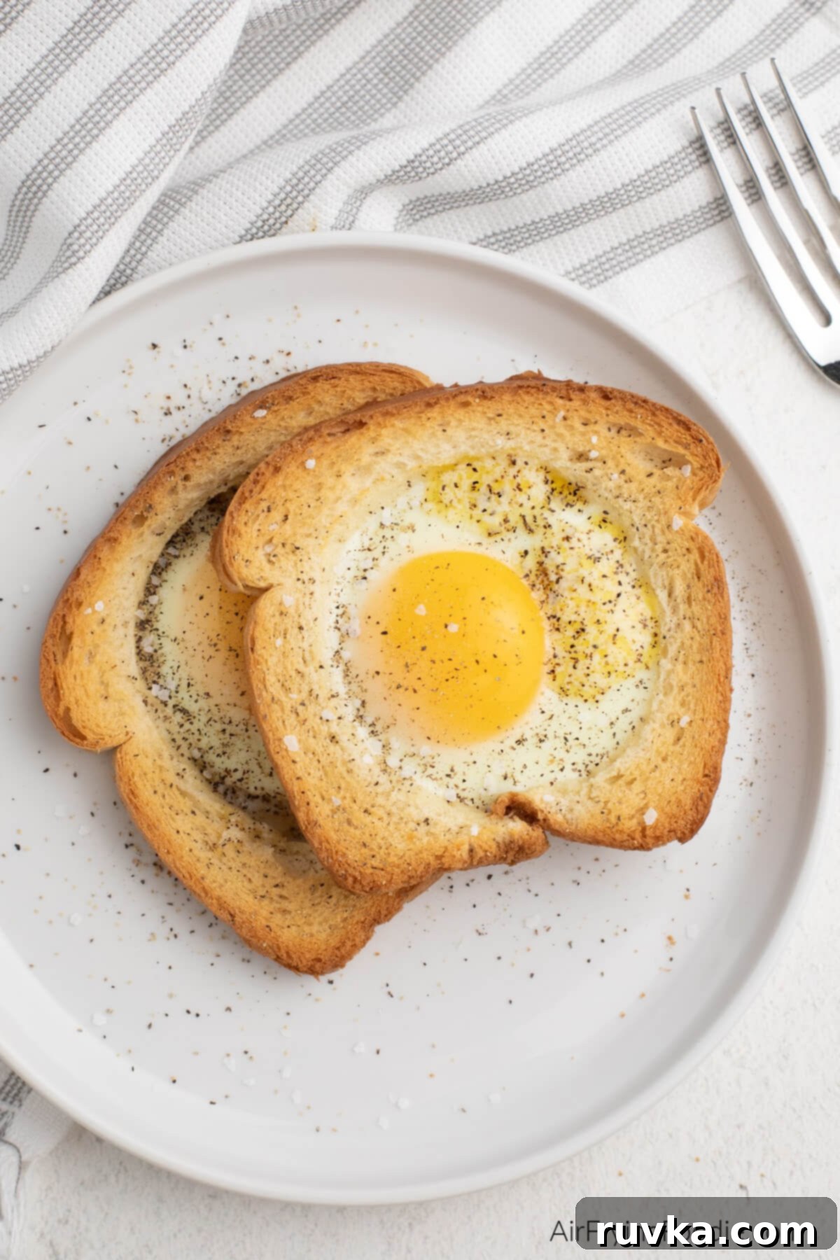 Crispy Air Fryer Egg Toast Baskets 2 Air fryer eggs in a basket, seasoned with salt and pepper and ready to serve. On a white plate.