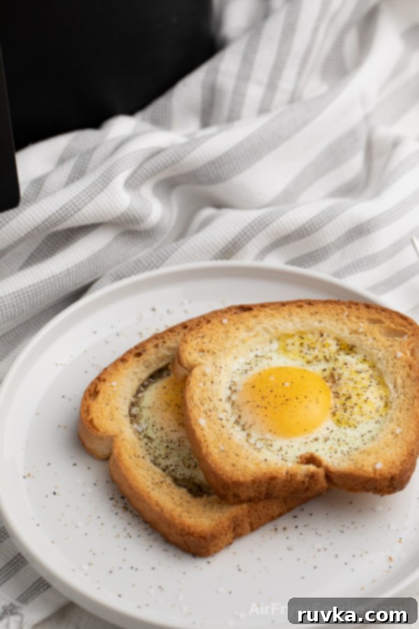 Crispy Air Fryer Egg Toast Baskets 4 Eggs in a basket on a white plate with salt and pepper sprinkled over the top. Black Air Fryer in the background.