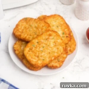 Golden Crispy Air Fryer Hash Browns 8 Golden brown and crispy hash brown patties on a white plate, served with a side of ketchup, a perfect and easy air fryer breakfast side.