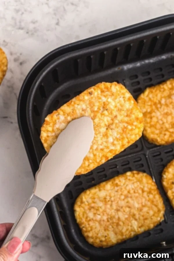 Golden Crispy Air Fryer Hash Browns 6 A spatula lifting a perfectly golden and crispy hash brown patty from the air fryer basket, ready to be served and enjoyed.