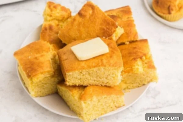 Air Fryer Cornbread Perfection 2 Cornbread cut up into squares and stacked on a white plate, topped with butter.