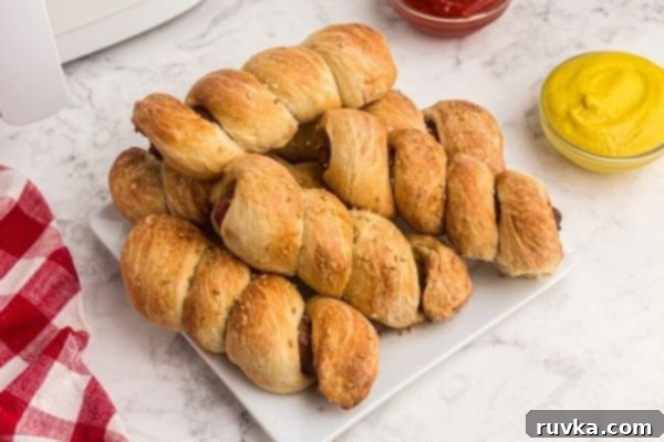 Crispy Air Fryer Pretzel Dogs 2 Golden pretzel wrapped hot dogs, served on a white plate with ketchup and mustard.