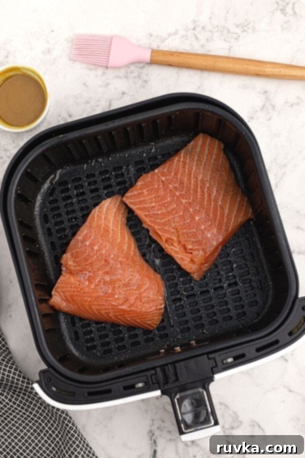 Effortless Air Fryer Honey Mustard Salmon 3 Two uncooked salmon fillets, seasoned with salt and pepper, placed directly into the air fryer basket, ready for glazing and cooking.