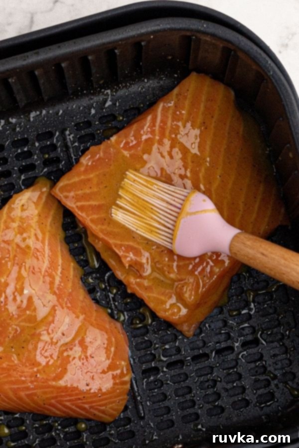 Effortless Air Fryer Honey Mustard Salmon 4 Uncooked salmon fillets resting in the air fryer basket, being carefully brushed with the golden honey mustard glaze, ready for cooking.