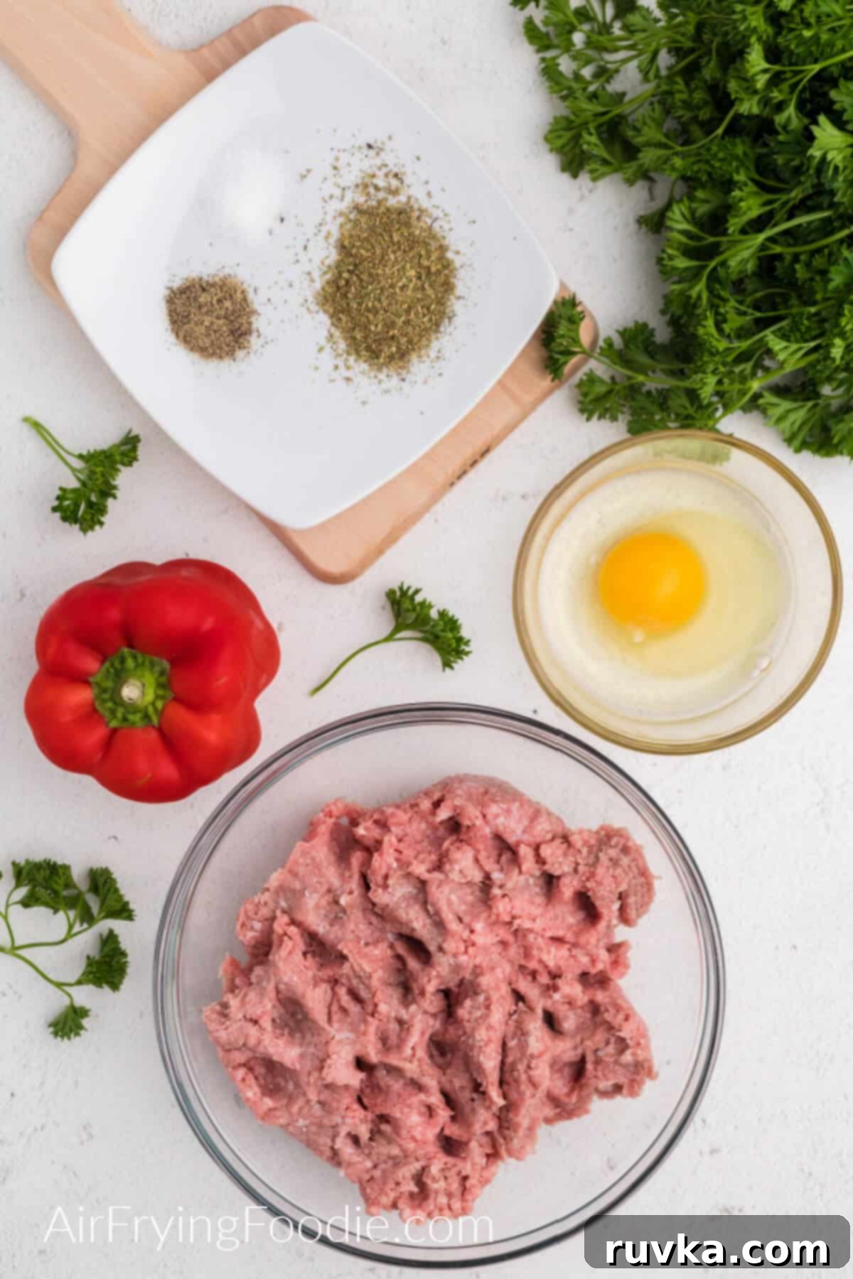 Crispy Air-Fried Turkey Meatballs 4 Red bell pepper, ground turkey in a bowl, egg in a small bowl, and seasonings on a white plate, surrounded by fresh parsley.