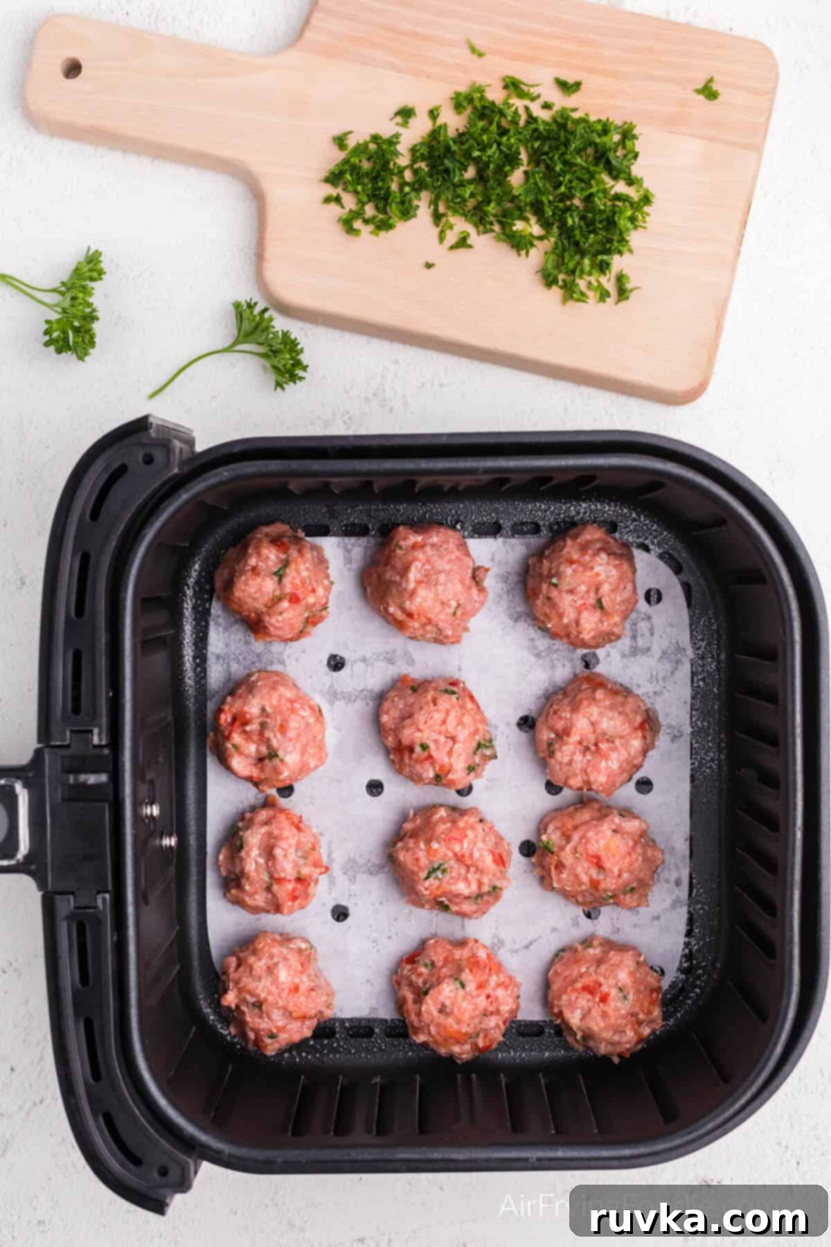 Crispy Air-Fried Turkey Meatballs 7 Turkey meatballs in the air fryer basket on a sheet of parchment paper. Ready to cook.